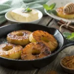 Caramelized tropical fried pineapple rings in a skillet with brown sugar and honey in background